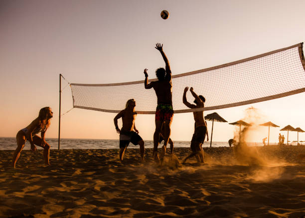 spielen sie volleyball am strand bei sonnenuntergang! - strand volleyball stock-fotos und bilder