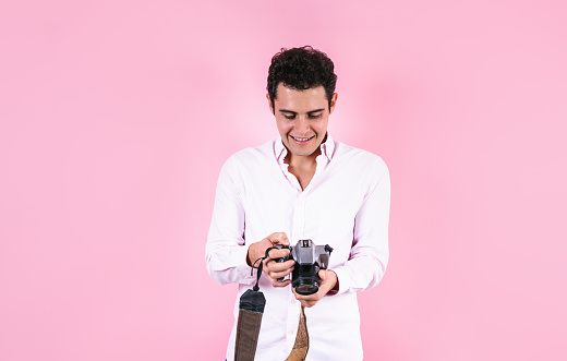 portrait of young hispanic man using a camera to take photos on pink background in Mexico Latin America