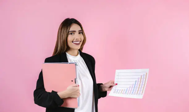 Photo of young hispanic business woman holding folders and smiling at camera on pink background in Mexico Latin America