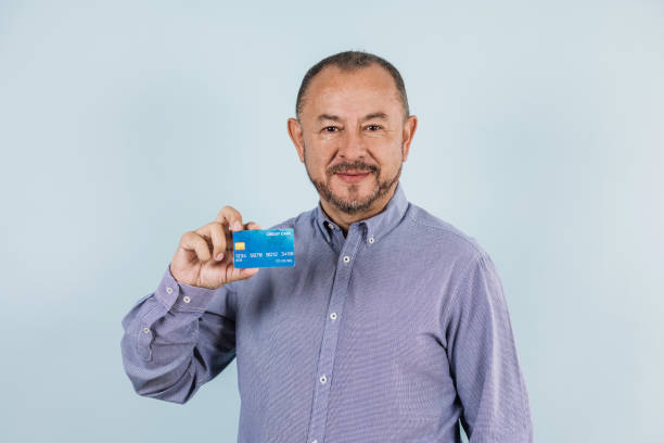 портрет латинского пожилого мужчины с кредитной картой на синем фоне в мексике латинская америка - mexico only men senior men mature men стоковые фото и изображения