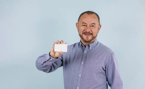 Photo of young hispanic business senior man holding blank card and smiling at camera on blue background in Mexico Latin America