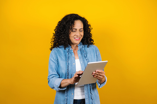 hispanic adult business senior woman portrait holding digital tablet on yellow background in Mexico Latin America