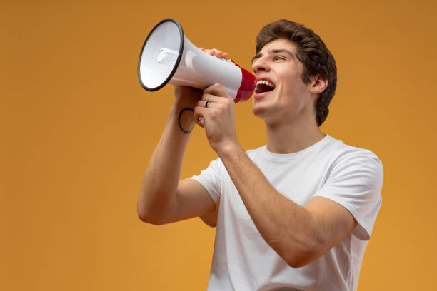 istock Young man shouting into megaphone making announcement against yellow background 1475225221