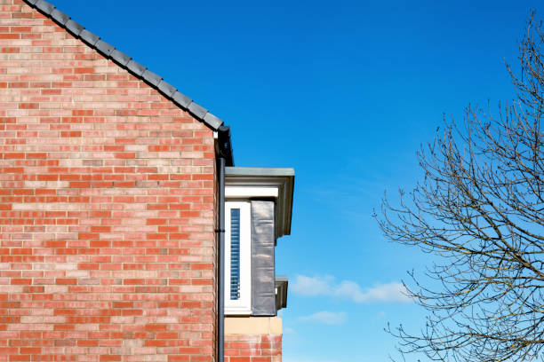 mattone rosso del tetto della casa sopra il cielo blu profondo, lato della casa dall'esterno con rami albero e cielo primaverile, modello di trama della parete di mattoni della casa inglese moderna - gable end foto e immagini stock