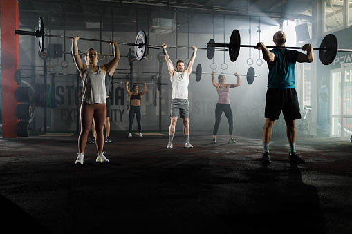 Group of athletic people exercising with barbells during cross training in a gym.