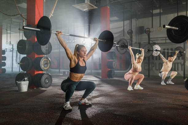 atletas que se exercitam com barras durante o treinamento cruzado em uma academia. - crouching barbell weightlifting weight training - fotografias e filmes do acervo