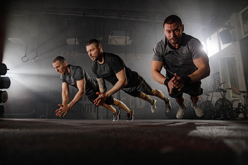 Group of young athletic men exercising push-ups while clapping their hands in a gym. Copy space.