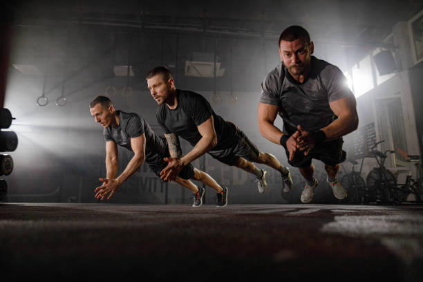 muscular build male athletes doing clap push-ups in a gym. - exercising men push ups muscular build imagens e fotografias de stock