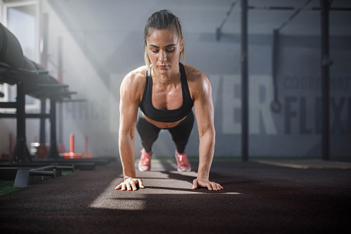 Young female athlete exercising push-ups with in a gym. Copy space.