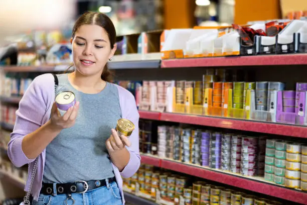 Photo of Young happy woman choosing canned pet food in pet shop