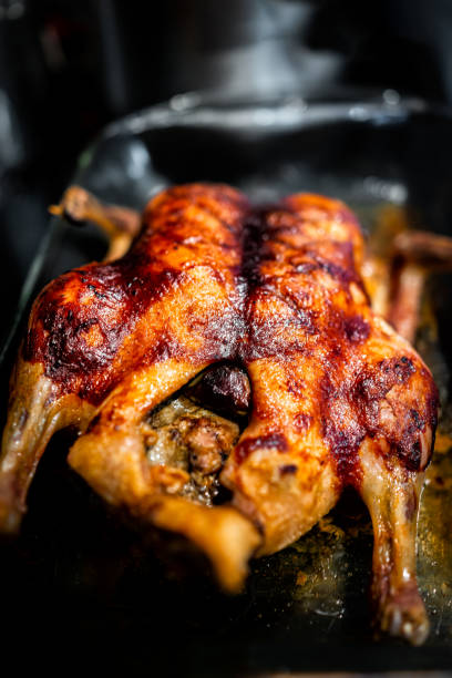istock Whole roasted duck poultry bird closeup vertical view on in glass pan for baking with crispy brown golden skin macro with texture 1475230408