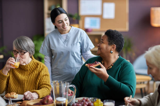 Young nurse assisting senior people during breakfast in retirement home
