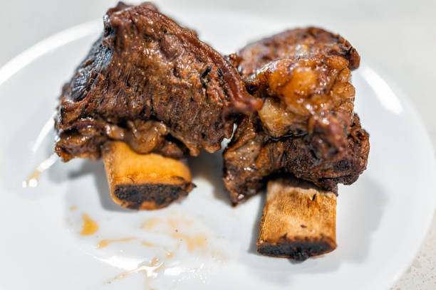 Roasted bone in beef short ribs cooked brown meat on white plate macro closeup with fat texture and nobody