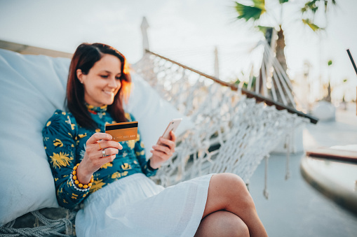 Relaxed woman in hammock using credit card for online shopping