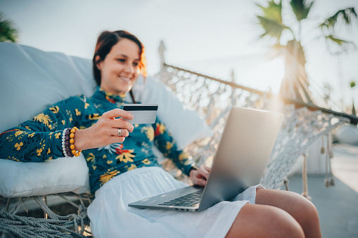 Relaxed woman in hammock using credit card for online shopping