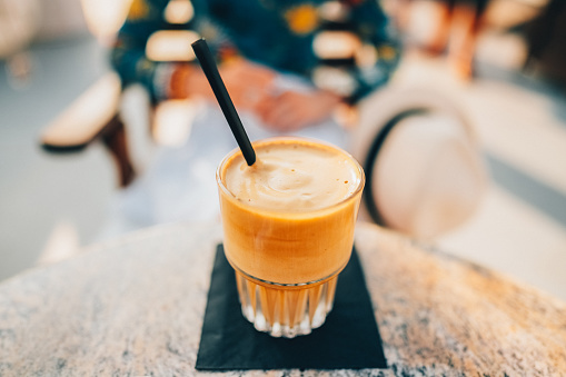 Close-up of drinking glass with coffee frappe and defocused woman at the background