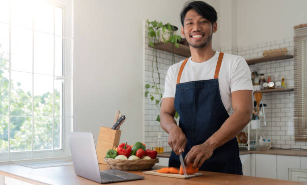 istock Man in kitchen looking at recipes on laptop while cooking 1475233053