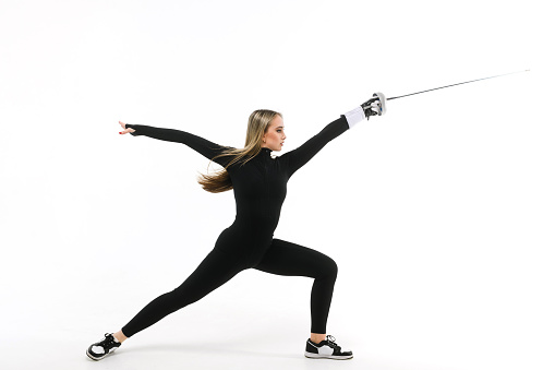 Teenage girl in a black tight-fitting jumpsuit practicing with a sword on a white background