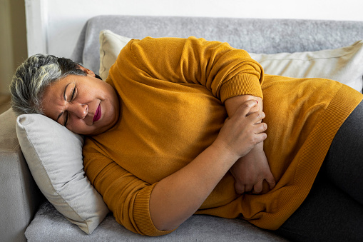 Woman suffering from stomach cramps on the sofa at home