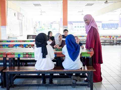 Schoolchildren enjoying lunch during breaktime in school while teacher supervising them