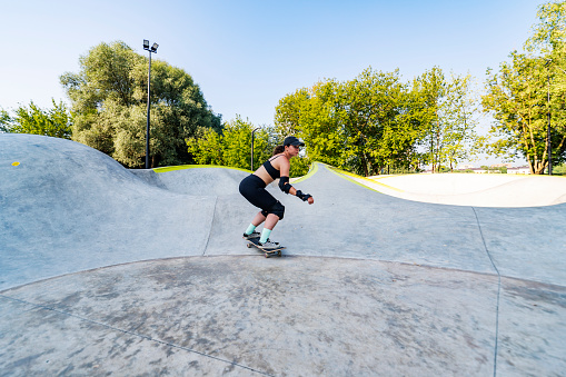 Young adult woman skateboarding in skate park at summer