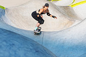 Young adult woman skateboarding in skate park at summer
