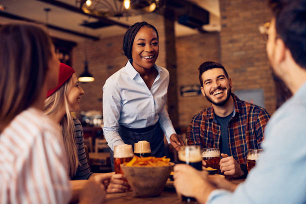 istock Cheerful African American waitress talking to her customers while serving them in a pub. 1475239831