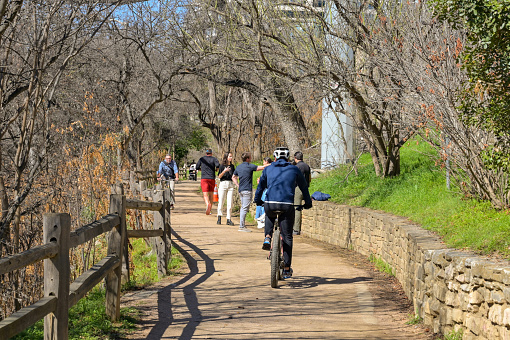 Austin, Texas, USA - February 2023: People walking and cycling on the path alongside the river near the city centre