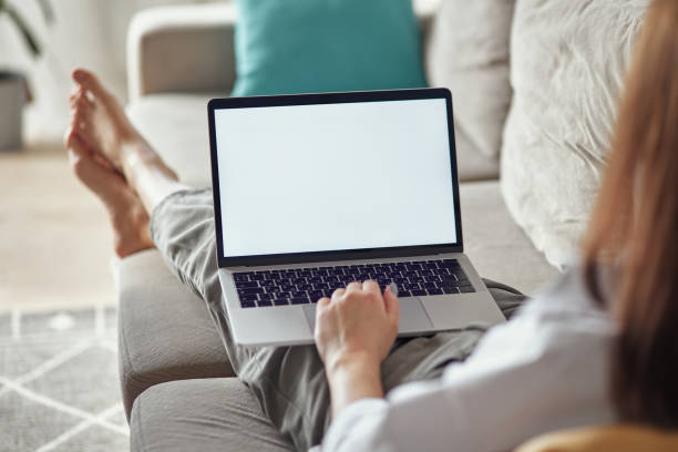 istock Mockup white screen laptop woman using computer lying on sofa at home, back view, focus on screen 1475252817