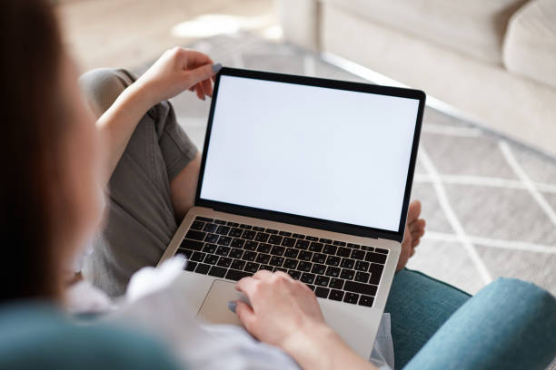 istock Mockup white screen laptop woman using computer sitting on armchair at home, back view, focus on screen 1475253107