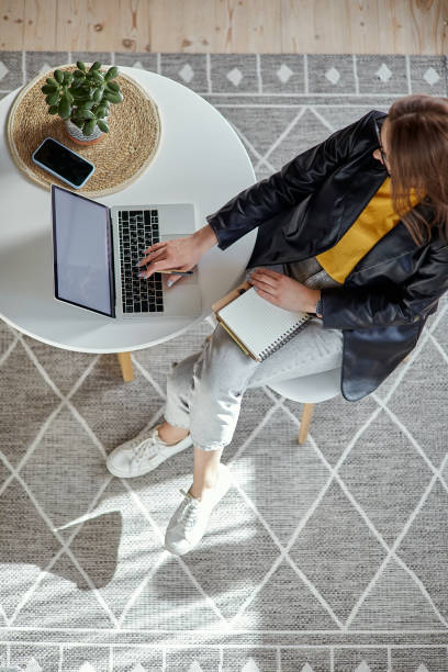 istock Young woman using laptop and making notes in notebook sitting at workplace at home, remote work top view 1475253660