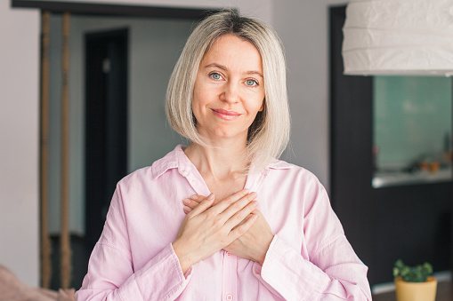Happy middle-aged woman hold hands at heart chest feel thankful, gratitude concept