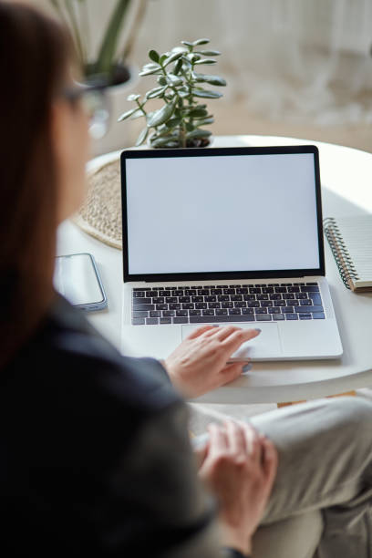 Mockup white screen laptop and mobile phone woman using computer sitting at table at home, back view