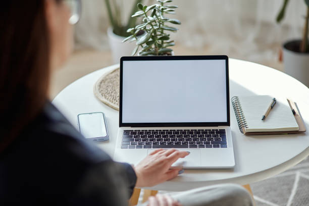 istock Mockup white screen laptop and mobile phone woman using computer sitting at table at home, back view 1475255539