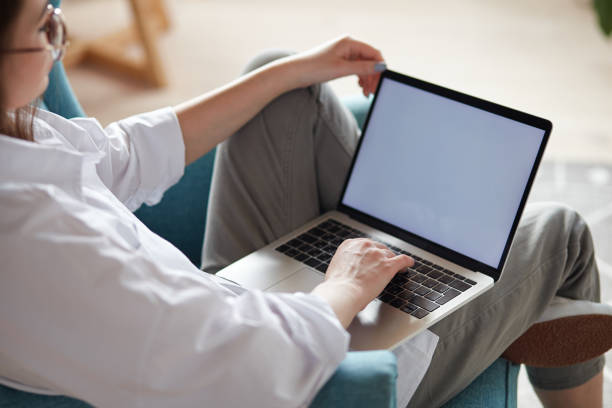 istock Mockup white screen laptop woman using computer sitting on armchair at home, back view, focus on screen 1475255676