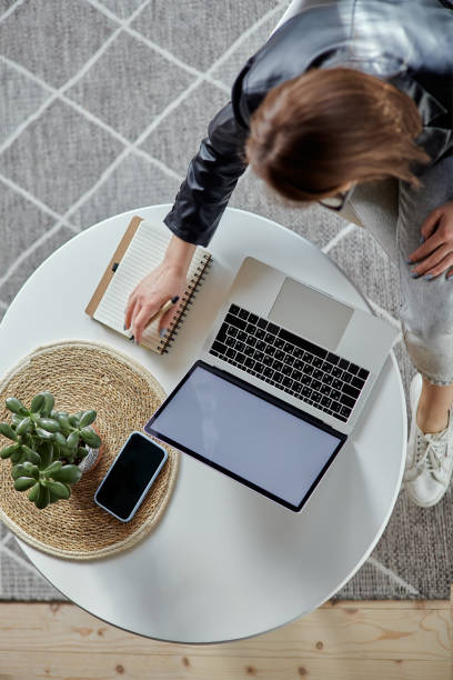 istock Young woman using laptop and making notes in notebook sitting at workplace at home, remote work top view 1475255727
