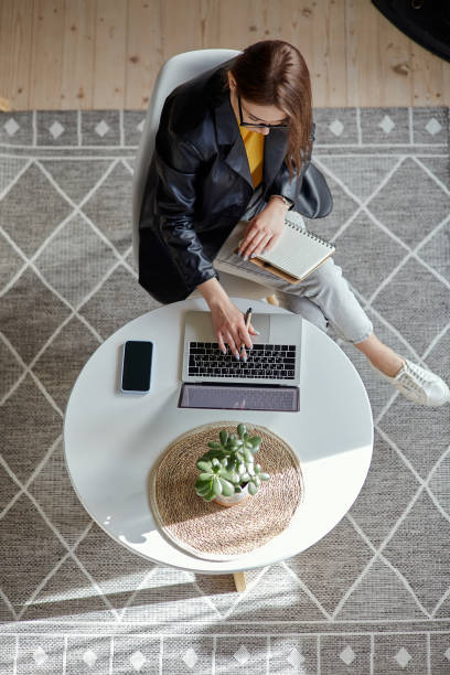 istock Young woman using laptop and making notes in notebook sitting at workplace at home, remote work top view 1475255900