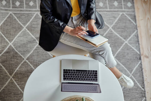istock Young woman using laptop and making notes in notebook sitting at workplace at home, remote work top view 1475255945