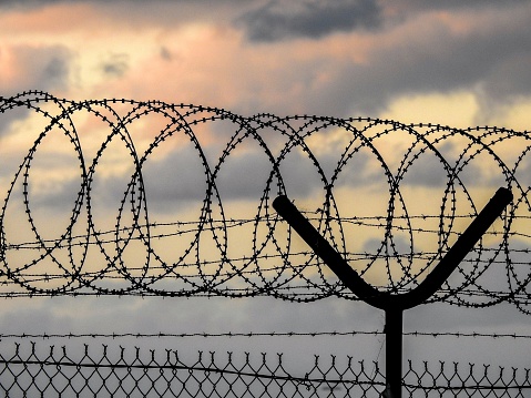 Razor wire, barbed wire and wire mesh fences surrounding Sydney Kingsford-Smith Airport.  This image faces west and the setting sun.  This image was taken near Shep's Mound on an overcast afternoon at dusk on 17 March 2023.