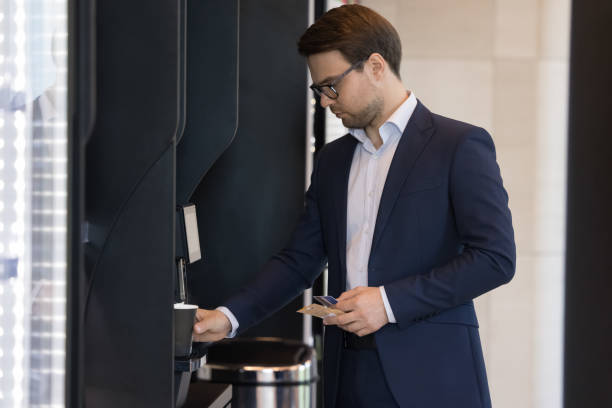istock Businessman in suit pours coffee uses vending machine in office 1475257399