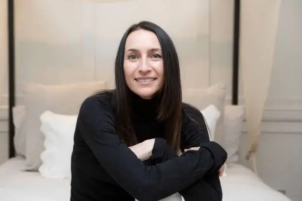 Relaxed and calm portrait of a woman in a bedroom. See is wearing a black polo neck jumper