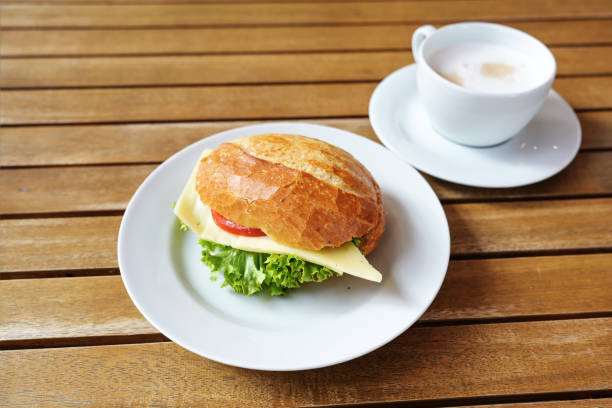 istock Fast breakfast in a cafe, bread roll with cheese, lettuce and tomato, plus a cup of coffee on a wooden table, copy space, selected focus 1475261503