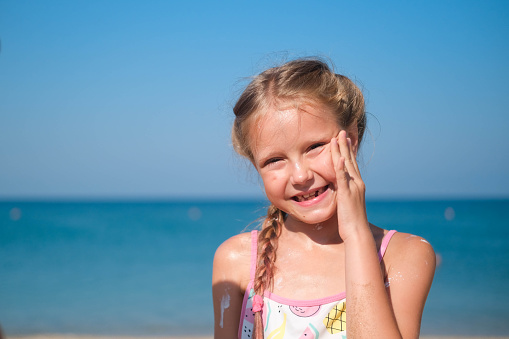 The girl smears her face with sun cream on the sea.