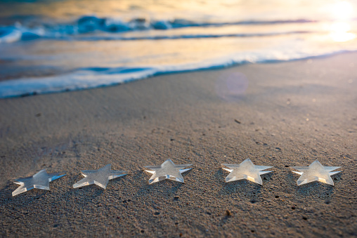 Five transparent stars on sandy beach at sunrise
