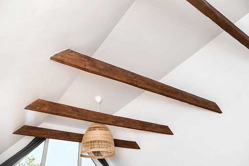 Stained brown decorative wooden beams in home living room white color ceiling. Nice modern contrast construction accent.