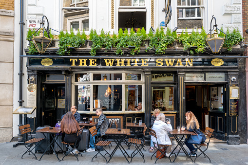 London, UK - 16 April 2022: The White Swan public house in New Row, Covent Garden, London. Customers are seated inside and outside of this late 17th, early 18th century Grade II listed building.