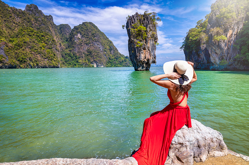 A tourist woman in a red dress looks at the famous sightseeing spot James Bond island at Phang Nga Bay, Phuket, Thailand