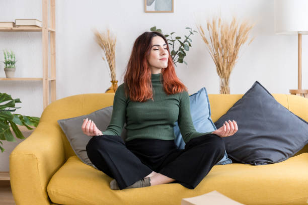 istock Young woman sitting on sofa relaxing and meditating 1475272022