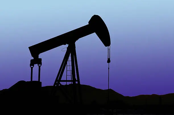 Oil Pump silhouetted against a mountain sunset with a gradient purple/blue sky