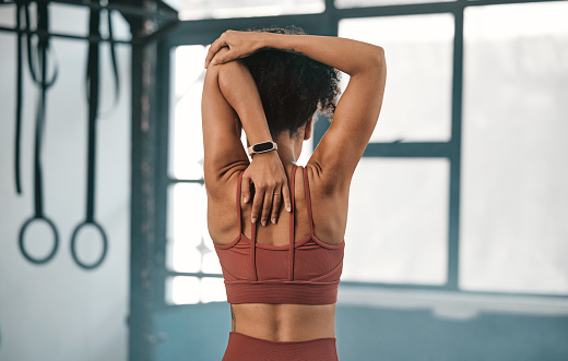 Fitness, back view or black woman in gym stretching to warm up body or relax arm muscles in workout exercise. Wellness, flexible or healthy sports girl training or exercising with focus or motivation